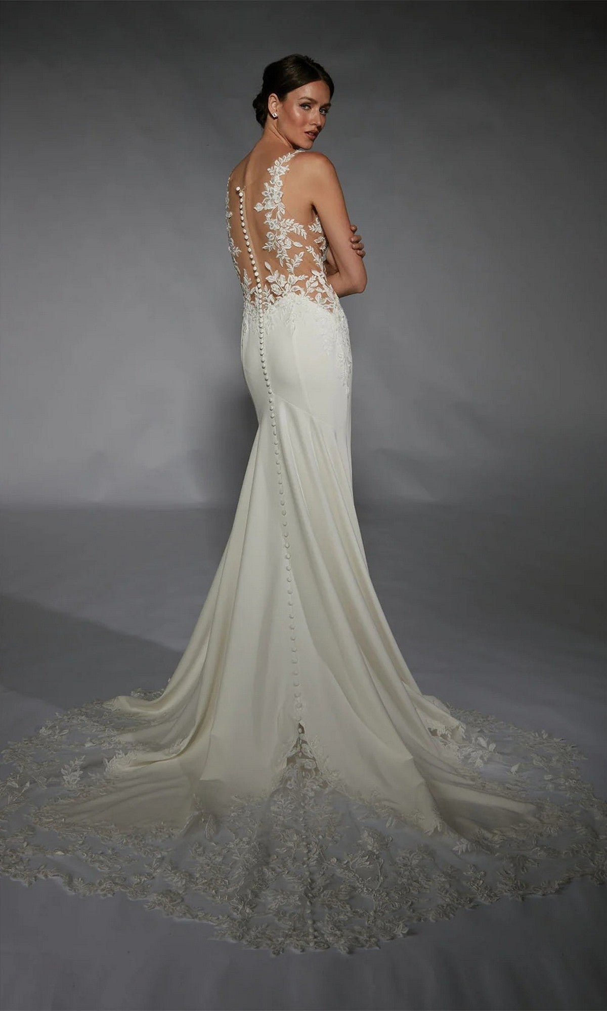 A woman in the Alyce 7117 Long White Dress, featuring an ivory hue, lace back, and elegant train, stands facing away and looks over her shoulder.
